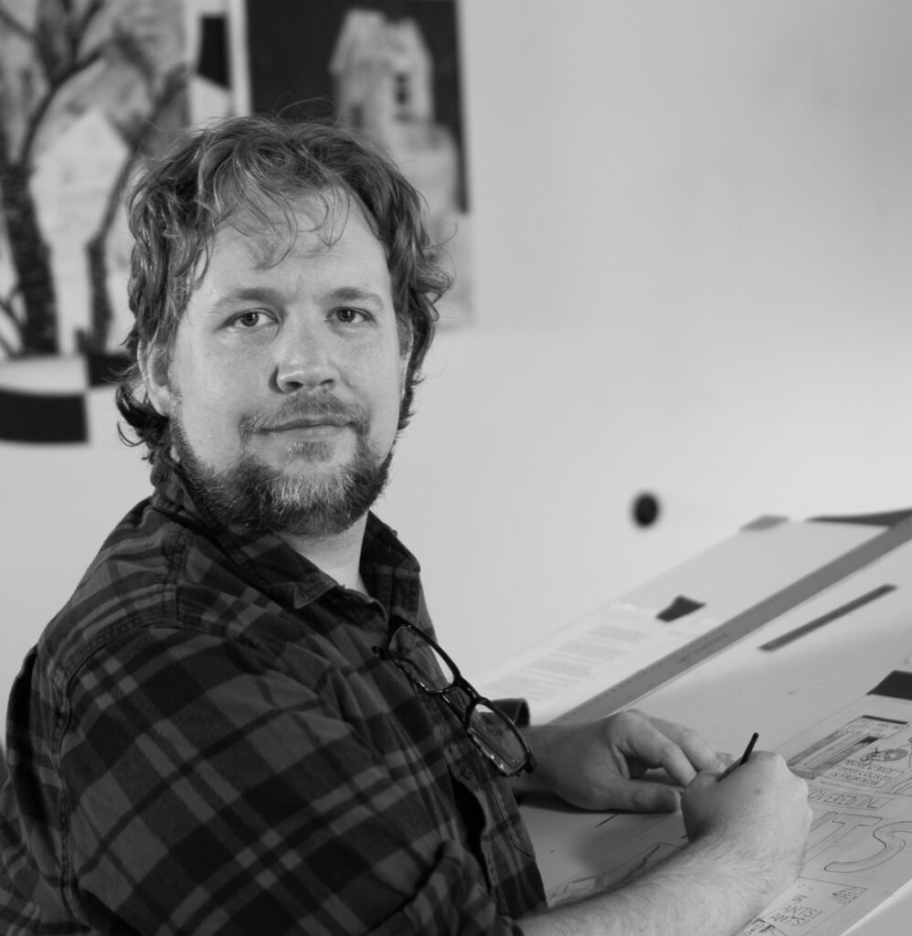 Kevin working at his drafting table, looking at the camera